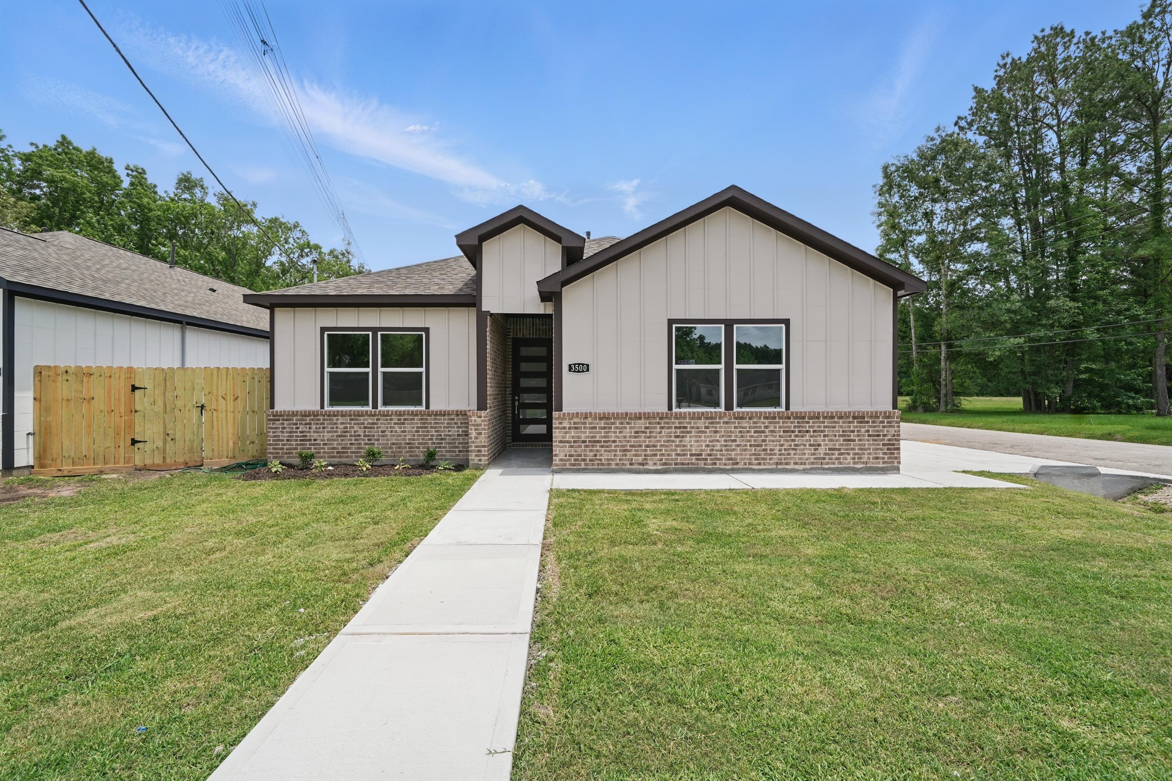 Modern single-story home with light siding, brick accents, and a concrete walkway on a green lawn.
